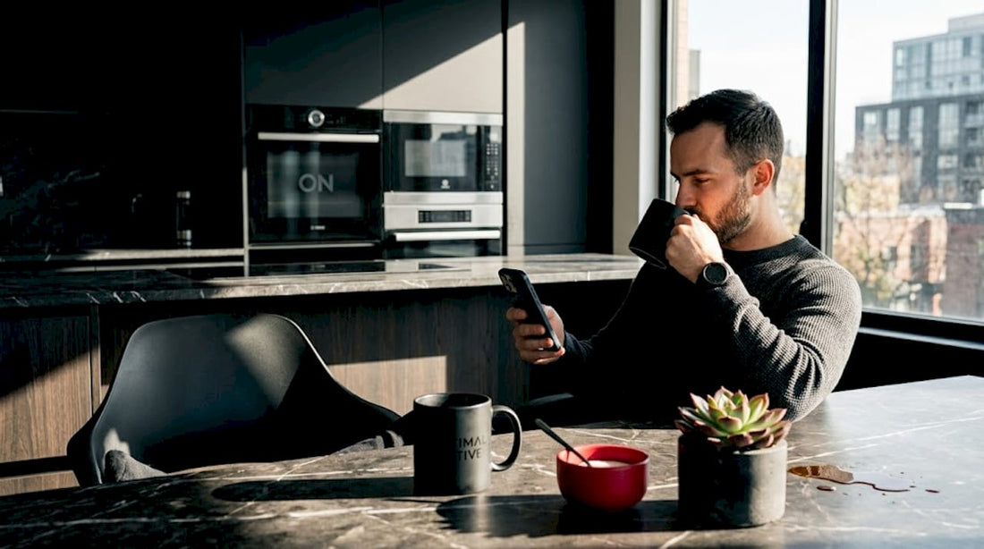 Un hombre disfruta de su café mientras hojea un libro en la cocina.