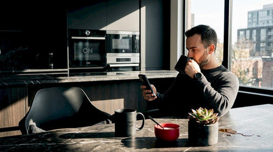Un hombre disfruta de su café mientras hojea un libro en la cocina.